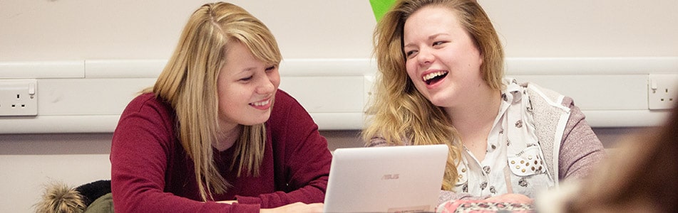students regarding a laptop and laughing